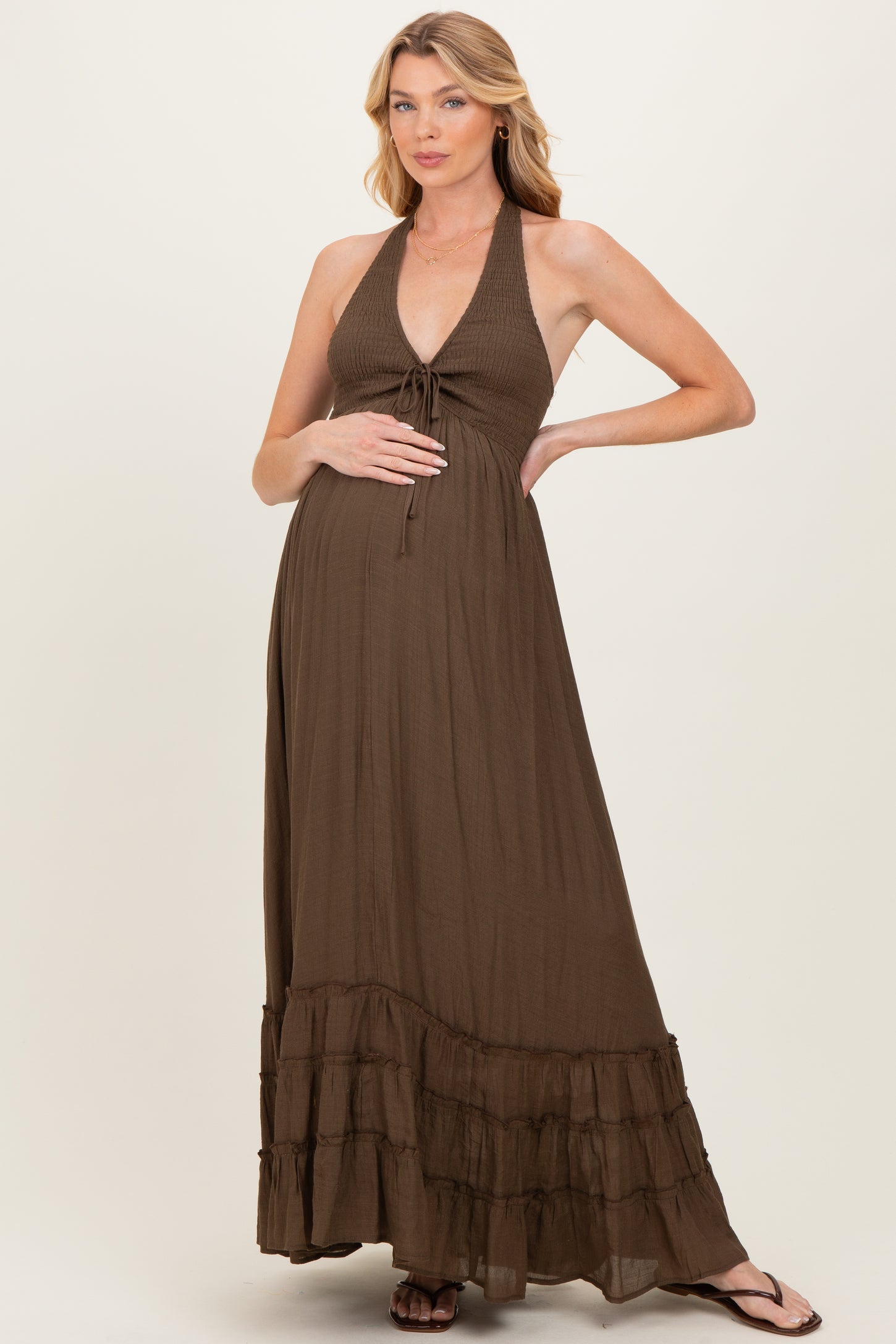 woman wearing a brown halter maternity maxi dress with tiered ruffle details and holding her baby bump