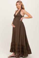 woman wearing a brown maternity maxi dress with a halter neckline and a tiered ruffle hem, holding her baby bump