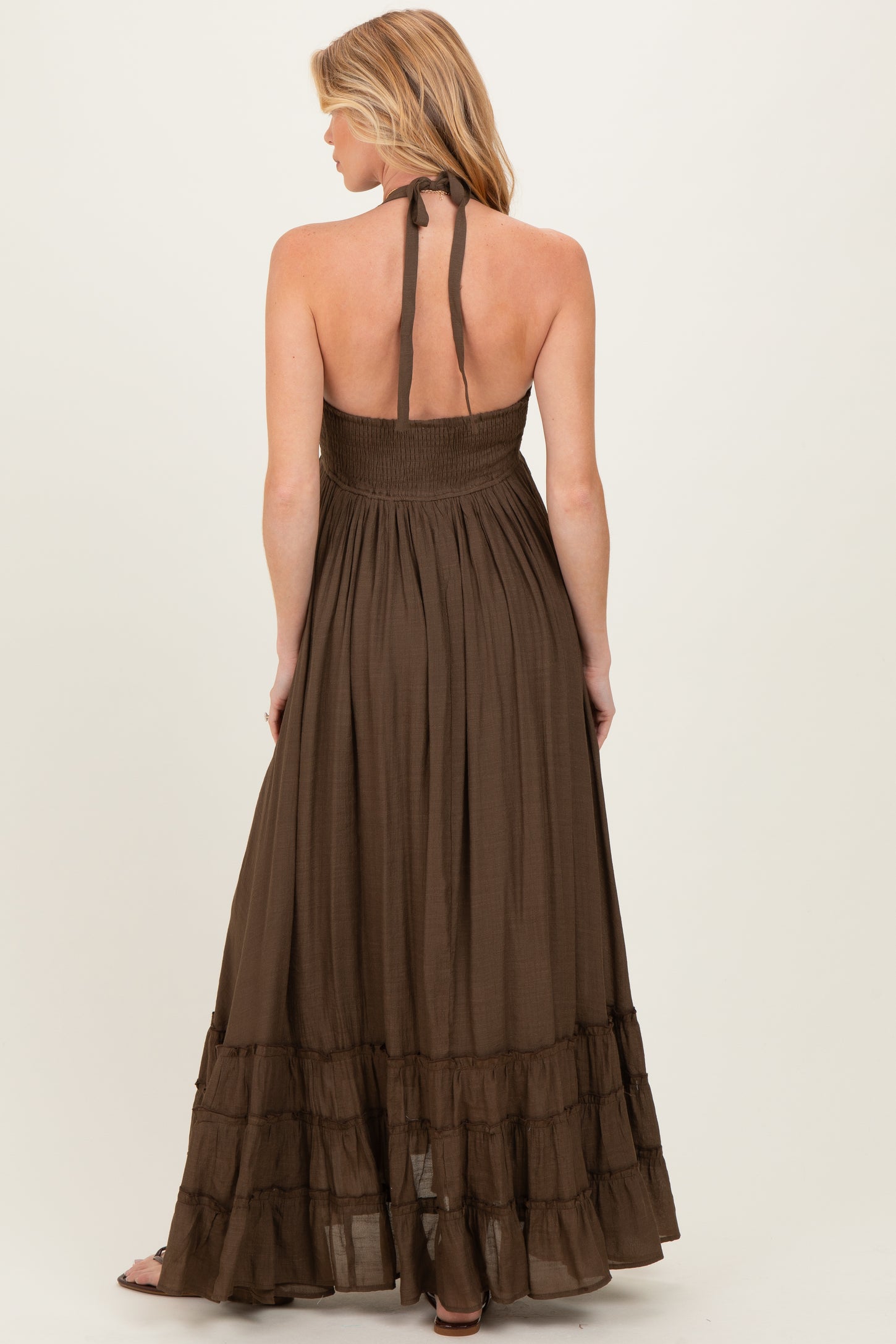 woman wearing a brown maternity maxi dress with a halter neck and ruffled hem, showing off her baby bump