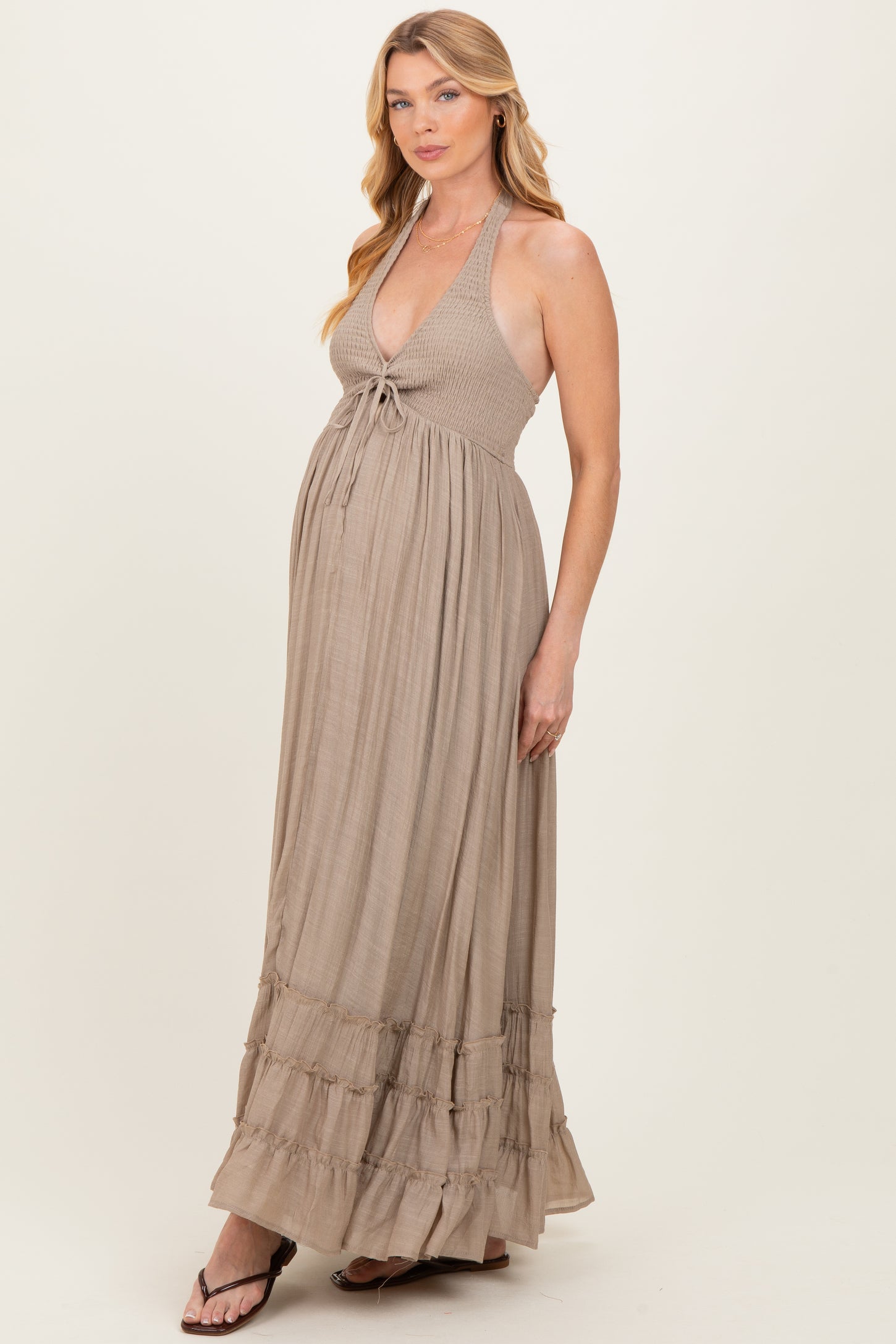woman wearing a beige halter tie maternity maxi dress with ruffle details and a visible baby bump