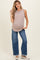 woman wearing a beige ribbed maternity tank top and loose blue jeans, holding her baby bump