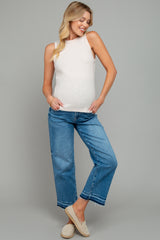 woman wearing a light beige ribbed maternity tank top and blue cropped jeans, showing her baby bump