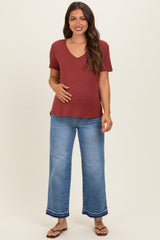 woman wearing a maroon v-neck maternity top and blue wide-leg jeans, gently holding her baby bump