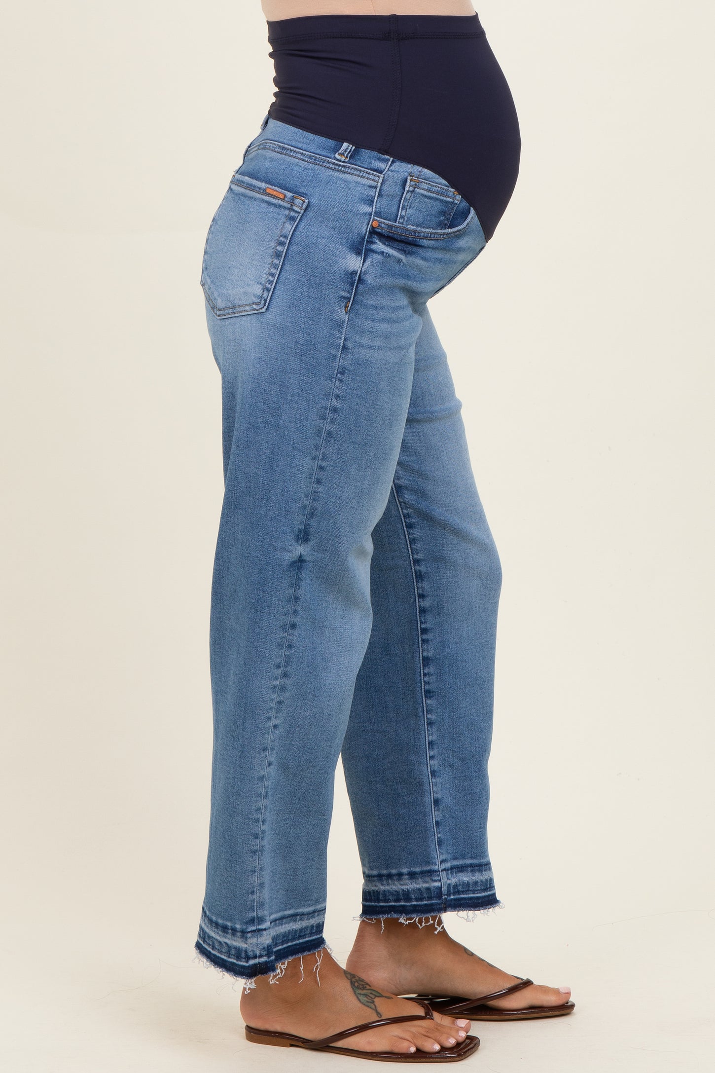 maternity wear in light blue distressed denim jeans with a navy blue belly panel and frayed hem, model showing baby bump