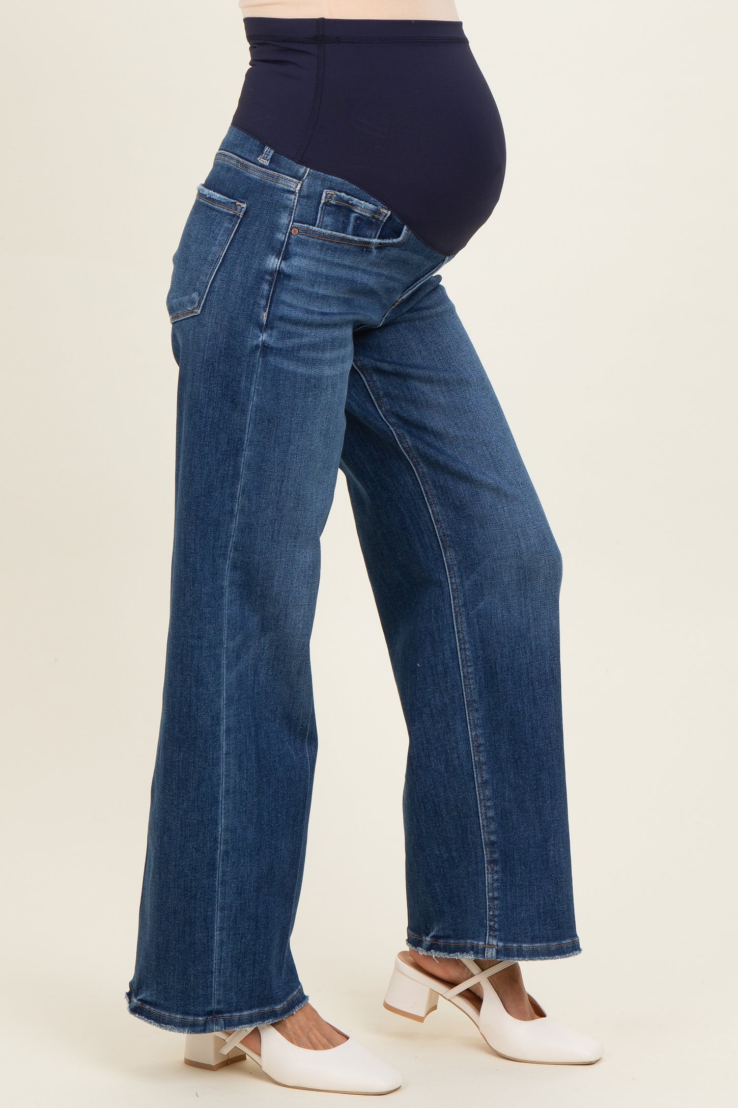 woman wearing blue maternity jeans with a stretchy waistband, showing a visible baby bump and white block-heeled shoes