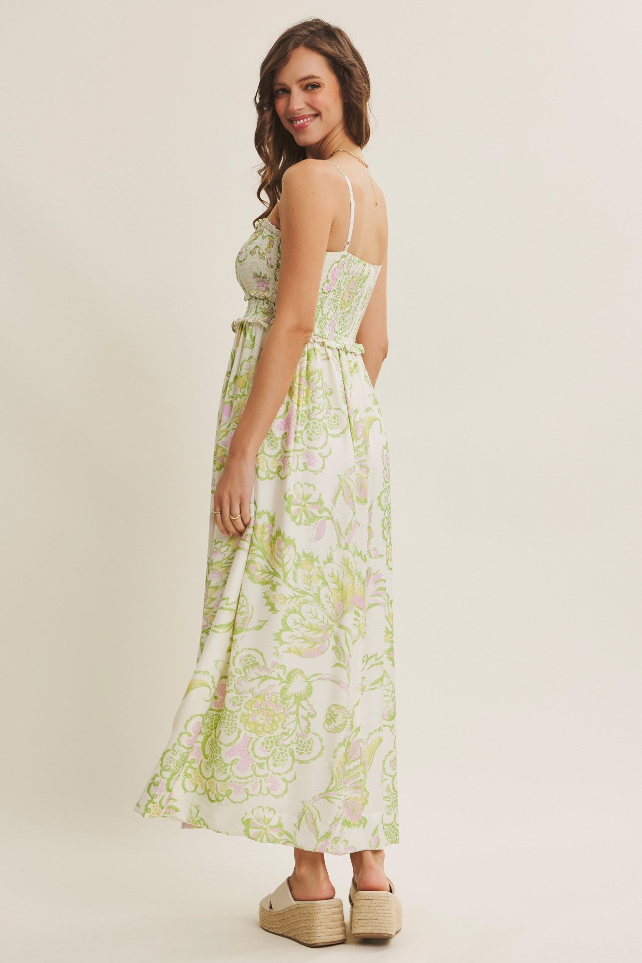woman wearing a white floral maxi dress with green and pink patterns and adjustable spaghetti straps, standing sideways