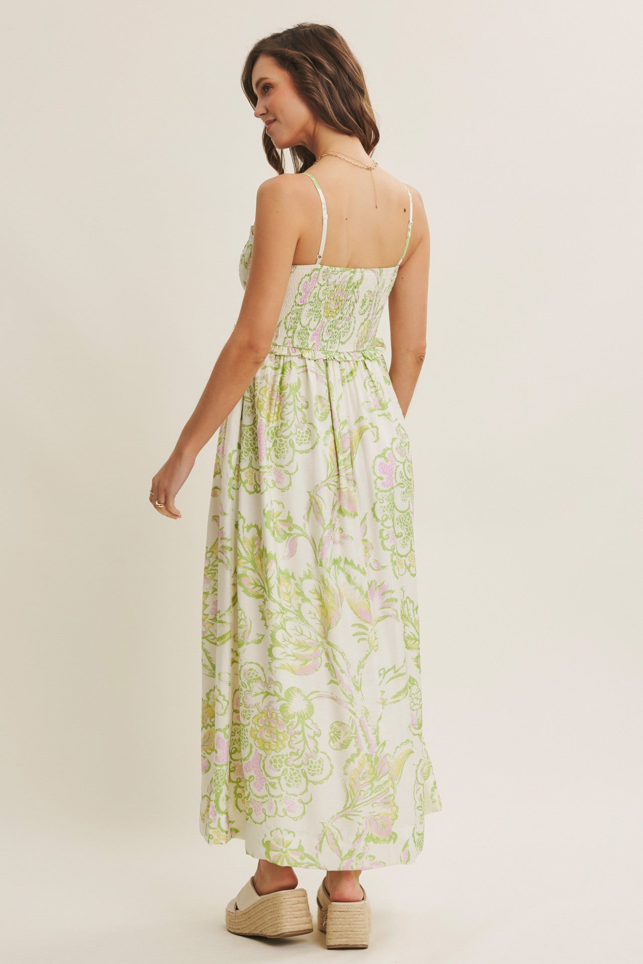 woman wearing a white maxi dress with green and pink floral print, showing the back view