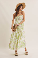woman wearing a floral print maxi dress with spaghetti straps and a straw hat, holding a woven bag