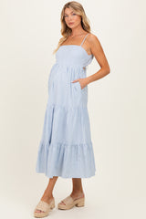 woman wearing a light blue striped maternity maxi dress with pockets and spaghetti straps, showcasing her baby bump