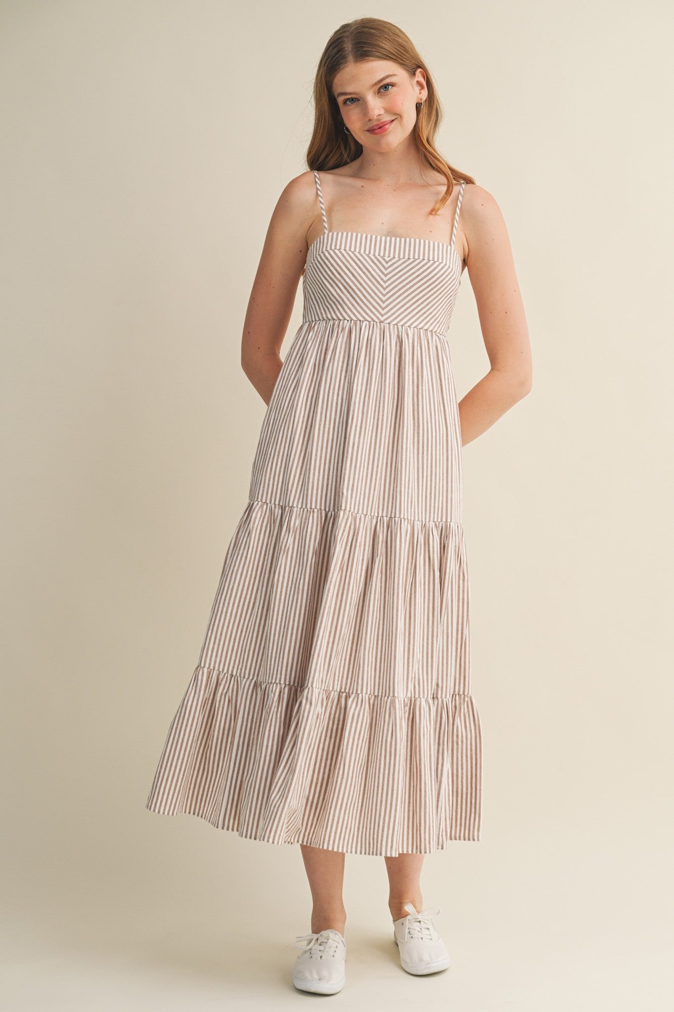 woman wearing a striped midi dress with thin straps and tiered skirt, standing with hands in pockets