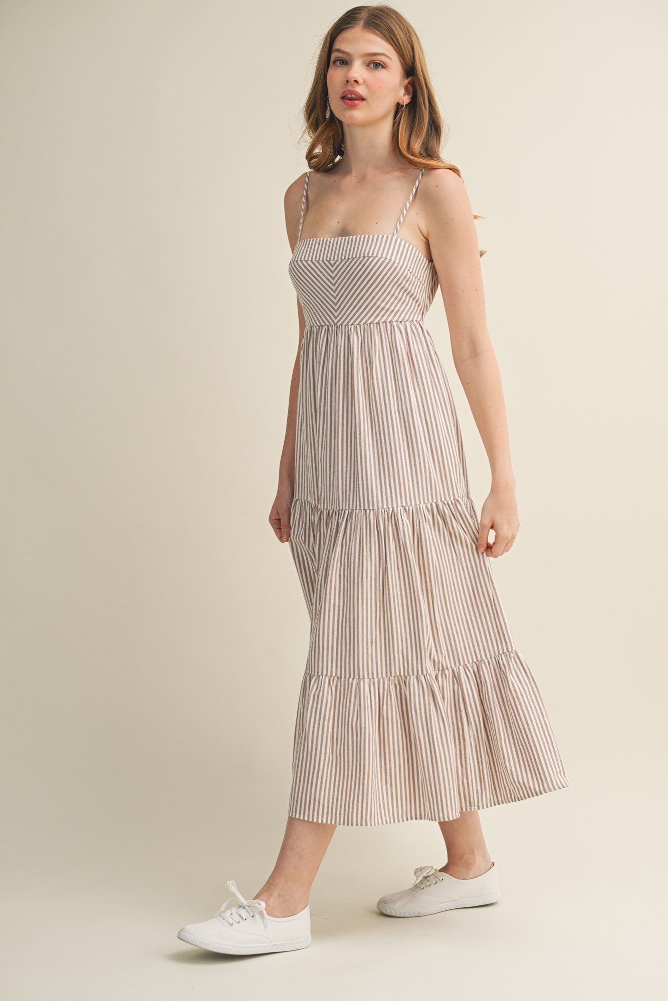 woman wearing a striped maxi dress with thin straps and tiered ruffles, paired with white sneakers