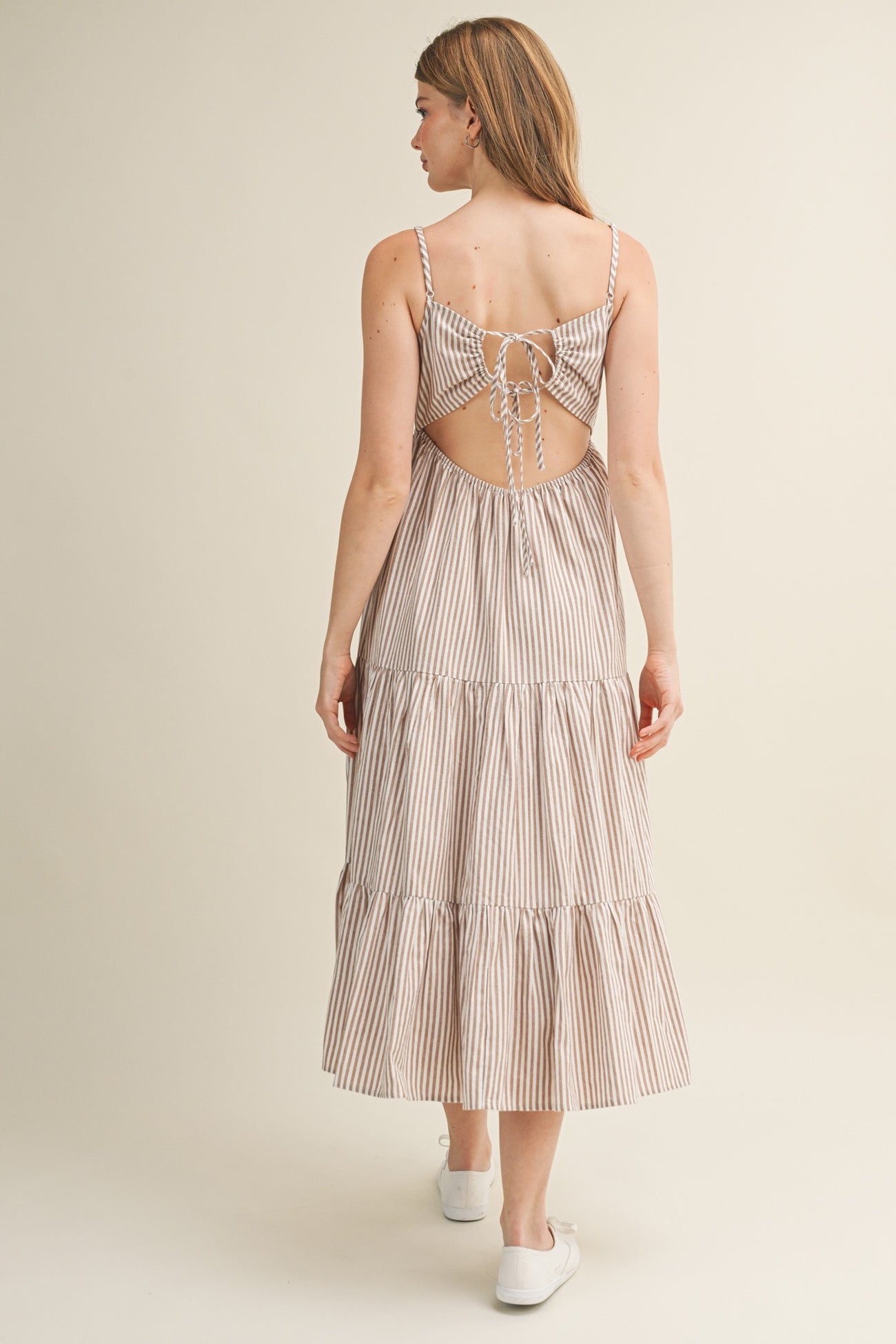 woman wearing a beige and white striped backless midi dress with adjustable ties and tiered skirt