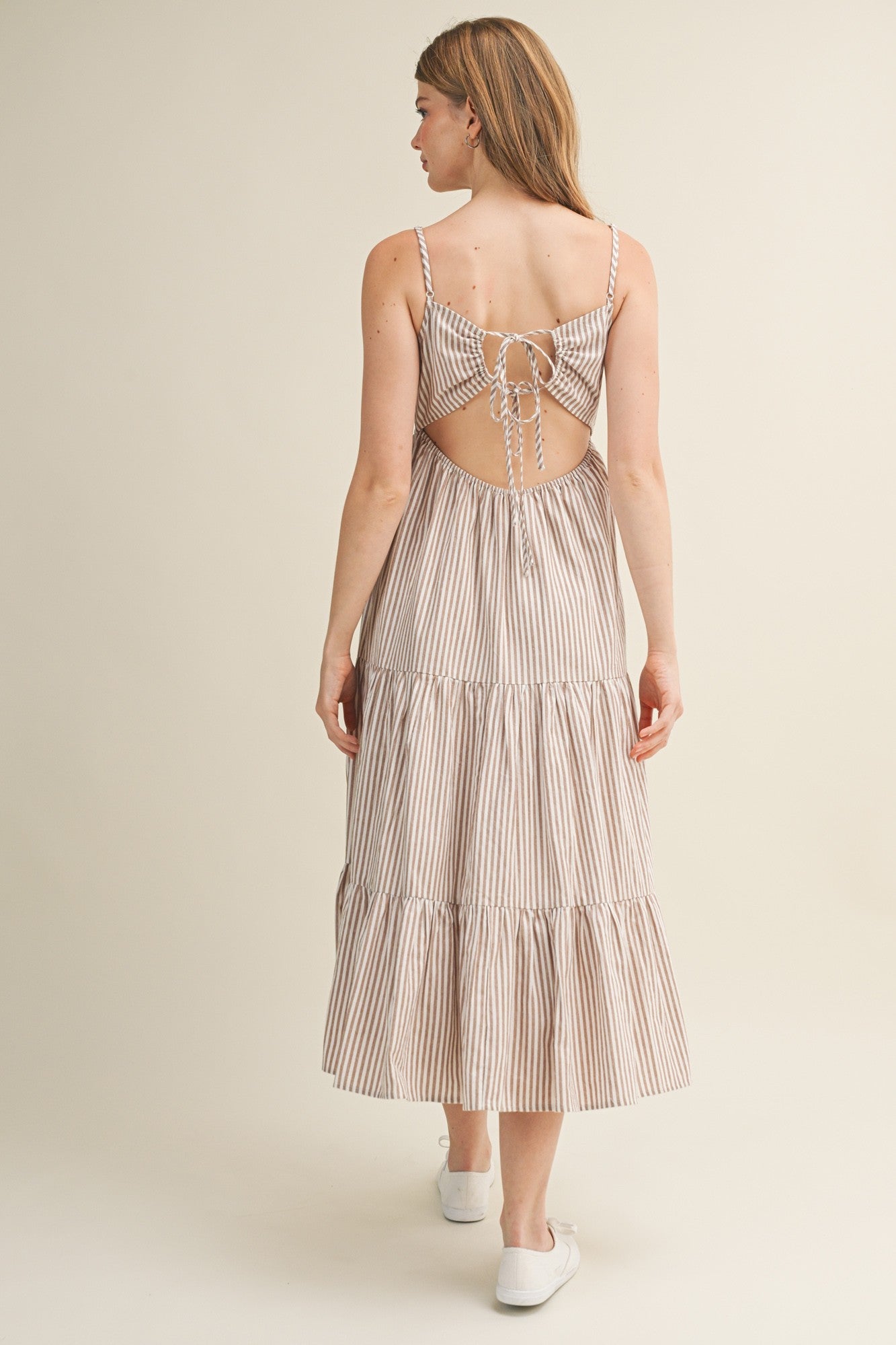 woman wearing a beige and white striped backless midi dress with adjustable ties and tiered skirt