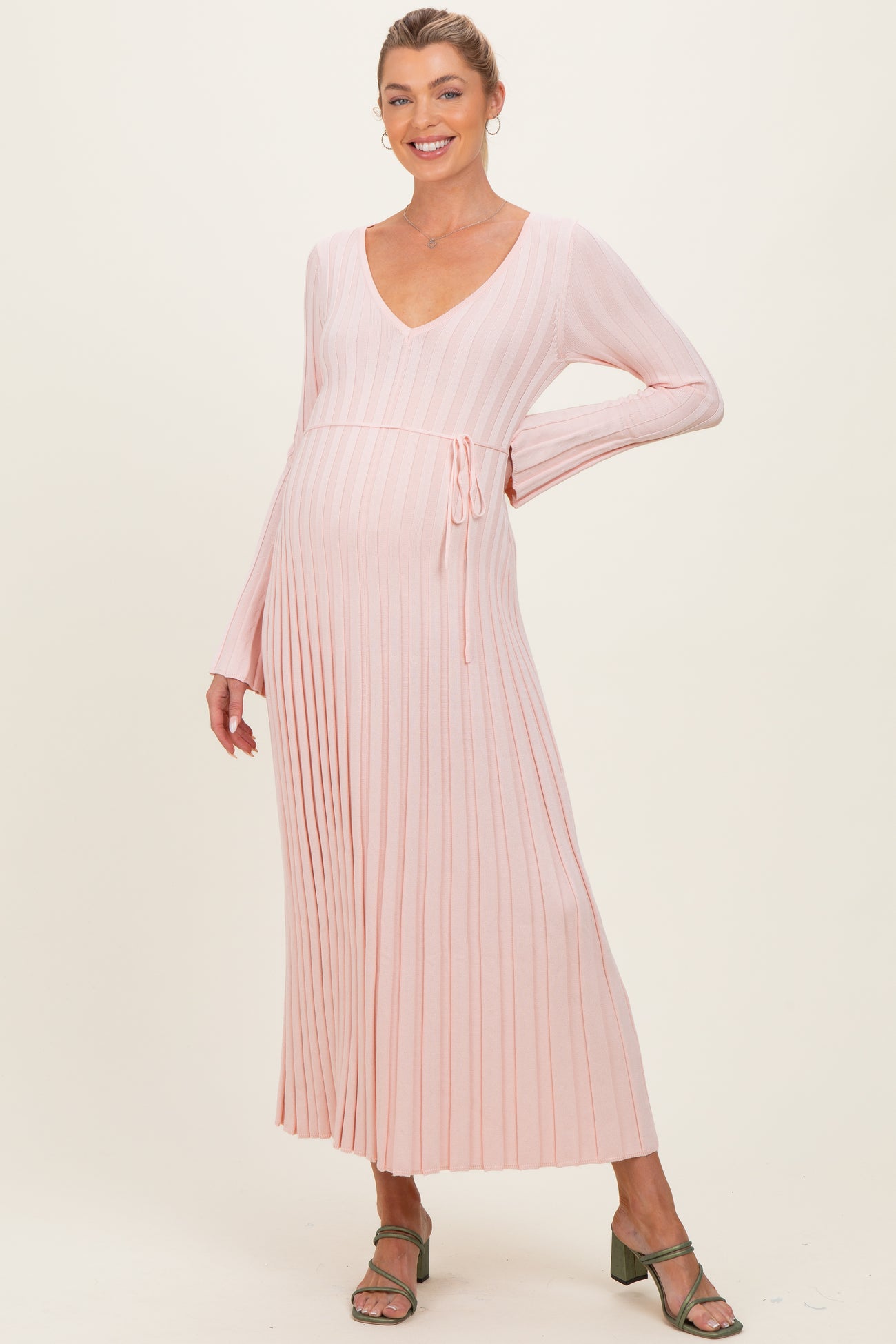 woman wearing a light pink long sleeve ribbed maternity dress with a tie waist and a visible baby bump