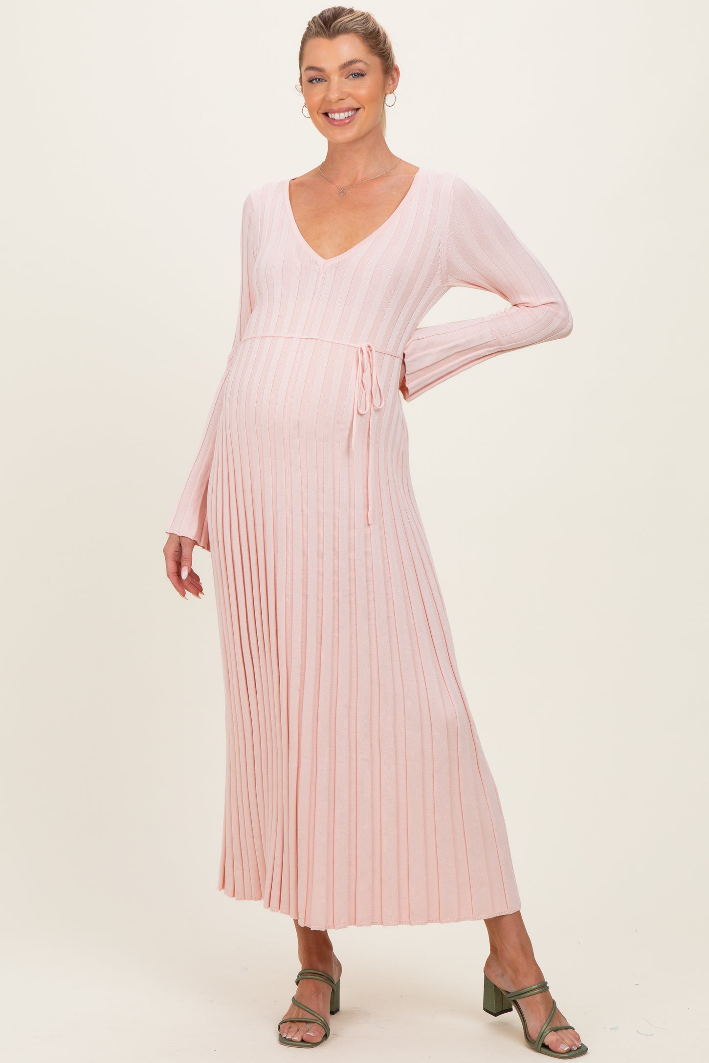 woman wearing a light pink long sleeve ribbed maternity dress with a tie waist and a visible baby bump