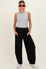 woman wearing a gray sleeveless top and black wide-leg maternity pants, standing with hands in pockets