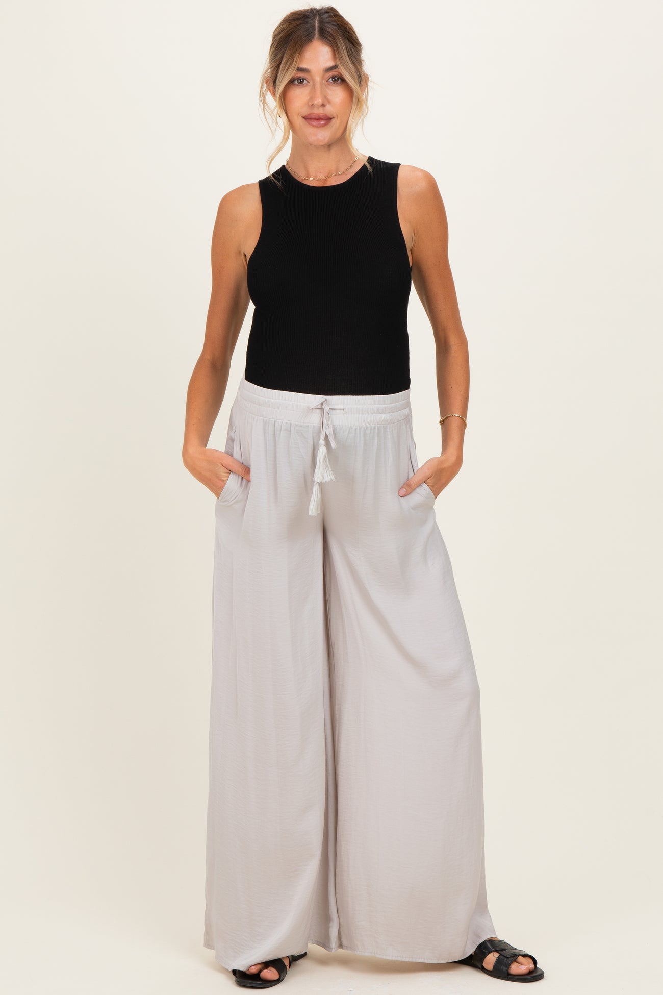 woman wearing a black ribbed maternity tank top and light grey wide-leg maternity pants with pockets and drawstring waist