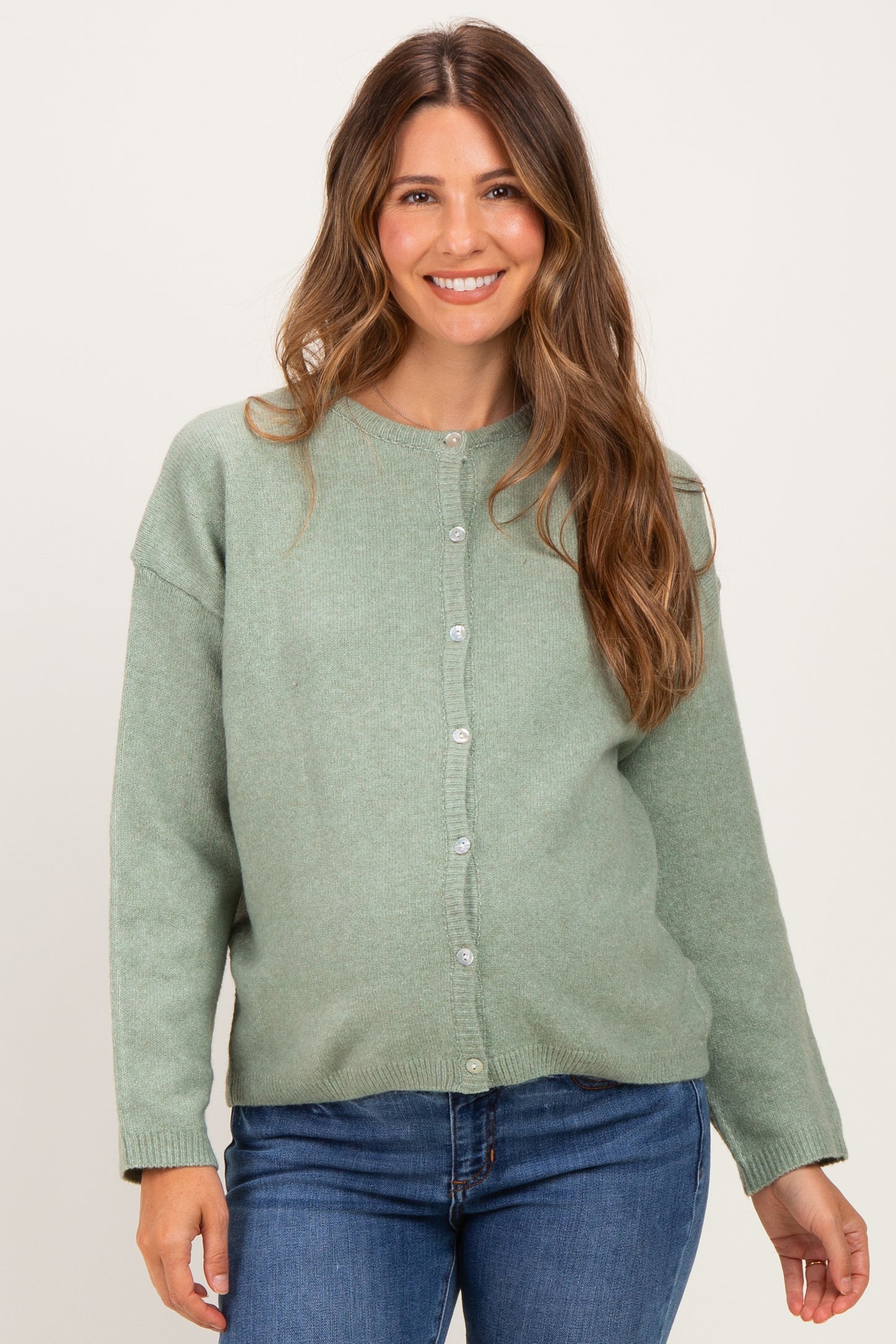 woman wearing a light green maternity cardigan with buttons, paired with blue jeans and showing a baby bump