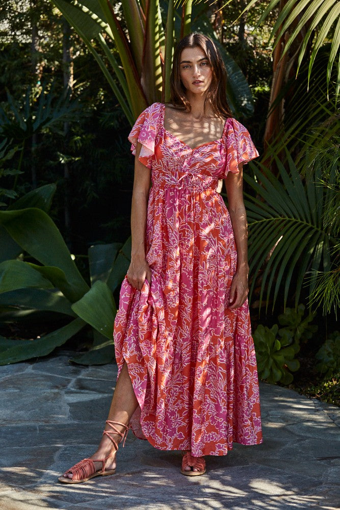 woman wearing a pink floral maxi dress with ruffled sleeves, standing among tropical plants
