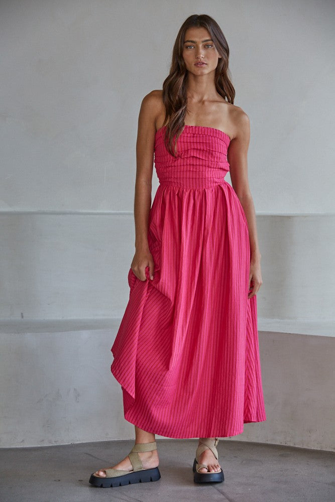 woman wearing a strapless pink maxi dress with a ruched bodice and flowy skirt, standing on a gray background