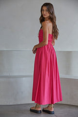 woman wearing a pink strapless maxi dress with smocked bodice and pleated skirt, standing with her back to the camera