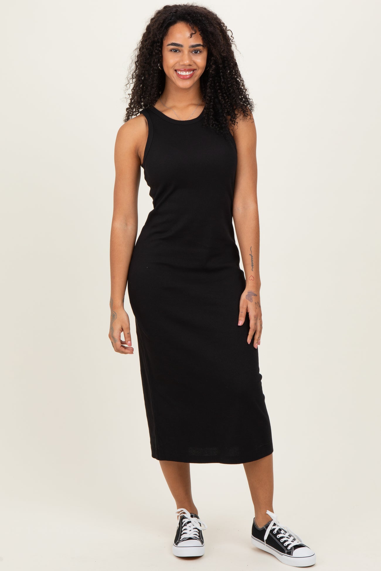 woman wearing a fitted black tank dress with a midi length and sneakers, standing confidently with a smile