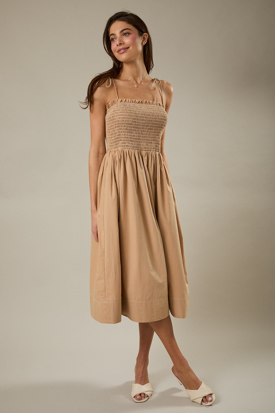 woman wearing a beige midi dress with a smocked bodice and thin straps, styled with white slip-on shoes