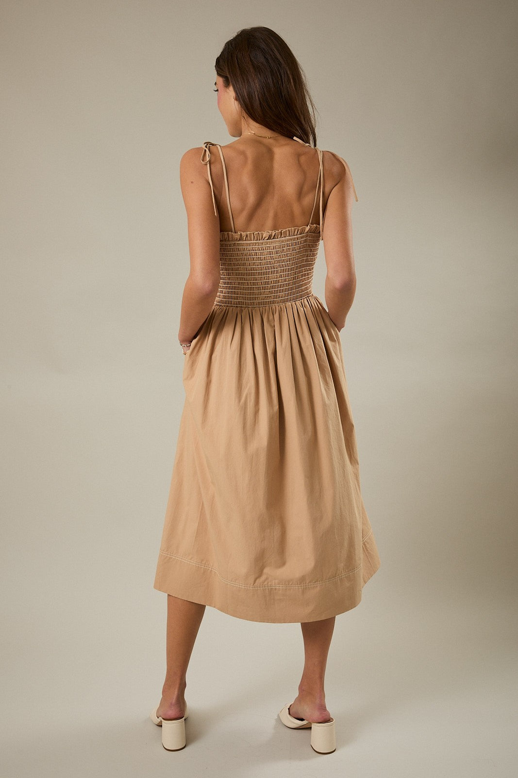 woman wearing a beige midi dress with a smocked back and tie straps, shown from the back