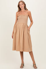 woman wearing a beige maternity dress with a smocked bodice and a full skirt, standing with hands in pockets