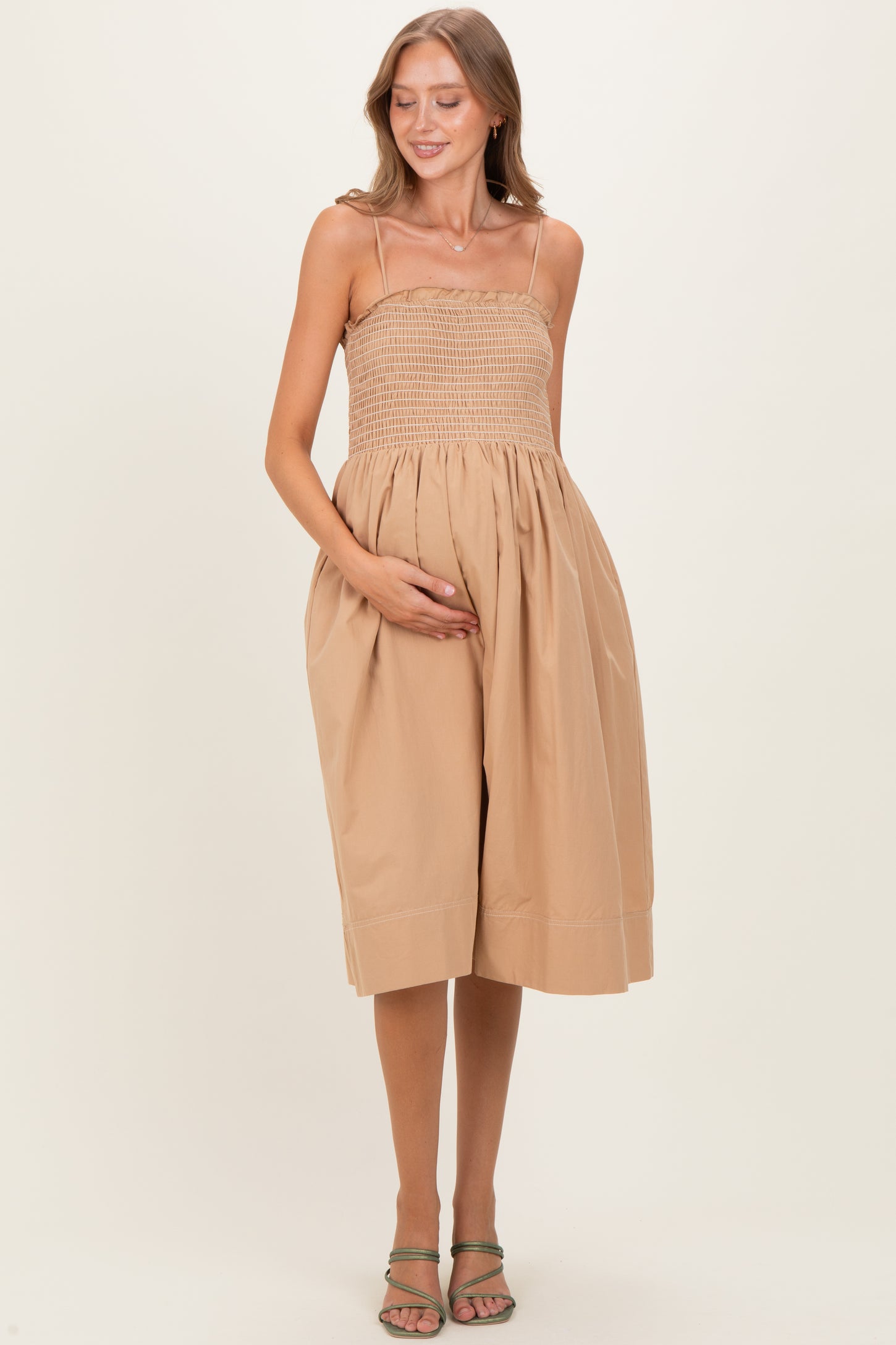 woman wearing a beige maternity dress with a smocked bodice and flowy skirt, holding her baby bump