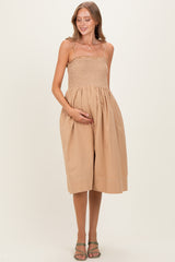 woman wearing a beige maternity dress with a smocked bodice and flowy skirt, holding her baby bump