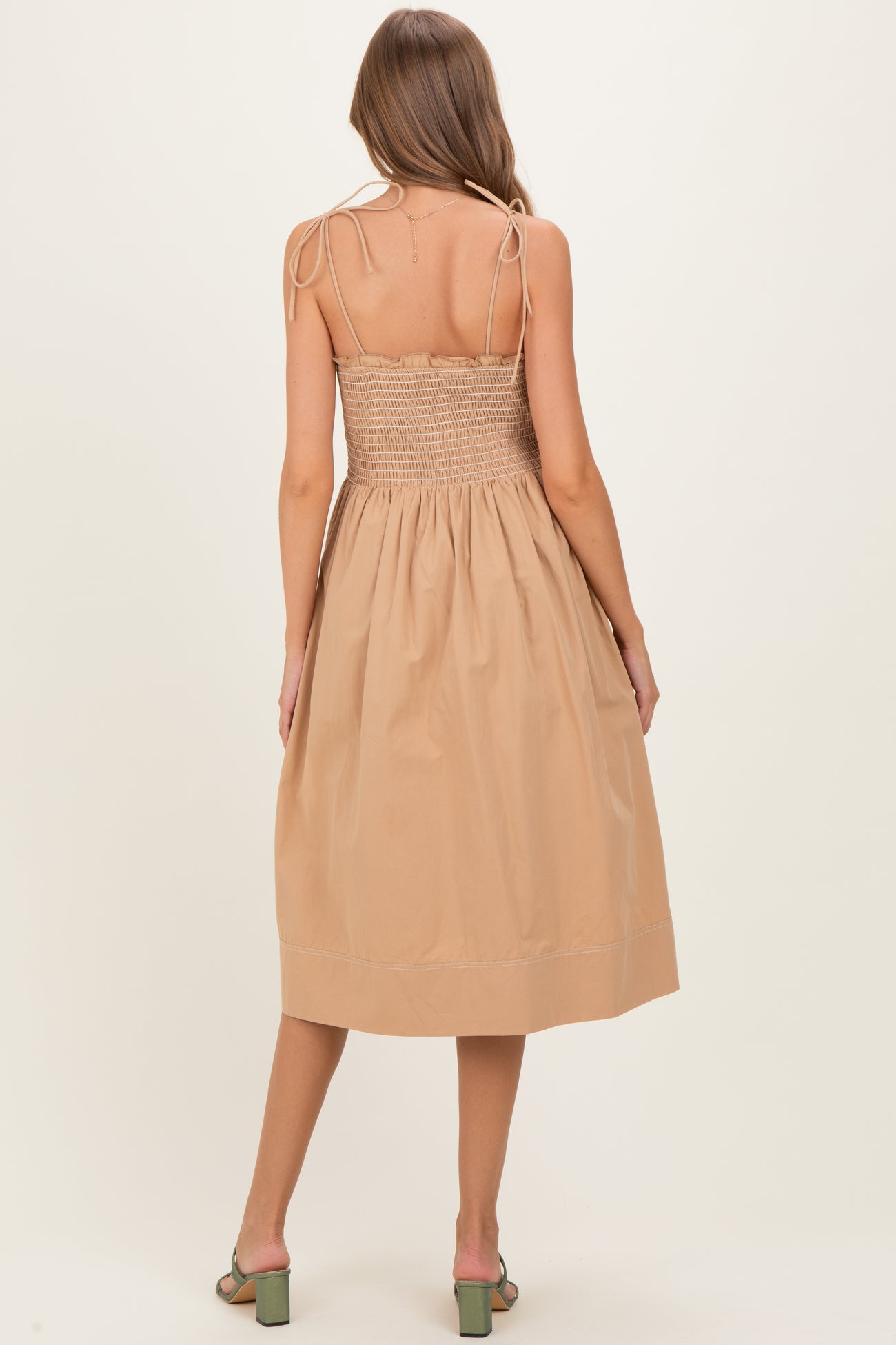 woman wearing a beige smocked back midi maternity dress with adjustable straps