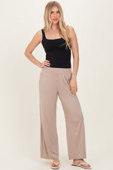 woman wearing a black fitted tank top and beige wide-leg pants, standing with one hand on her hip