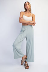 woman wearing a white crop top and light green wide-leg pants, standing with one leg slightly bent and hands on hips