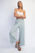 woman wearing a white crop top and light green wide-leg pants, standing with one leg slightly bent and hands on hips