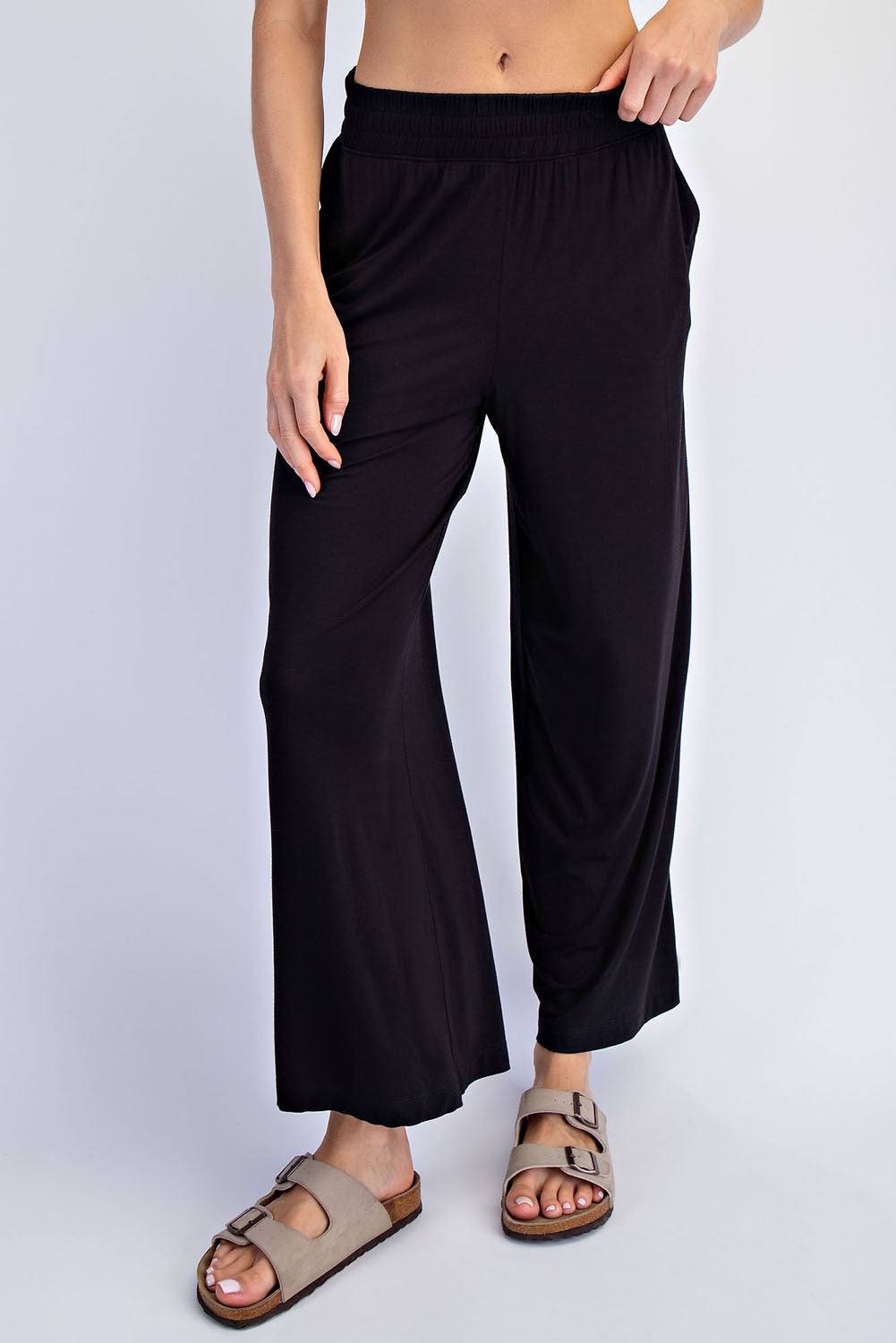 woman wearing black wide-leg pants with an elastic waistband and side pockets, paired with tan slide sandals