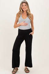 woman wearing a gray maternity tank top and black wide-leg maternity pants, holding her baby bump