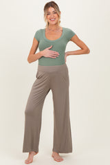 woman wearing a light green maternity top and beige maternity wide-leg pants while holding her baby bump