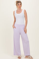 woman wearing a white ribbed tank top and lavender wide-leg pants, posing with hands in pockets