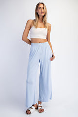 woman wearing a light blue wide-leg pants and a white crop top, standing with one hand on her hip