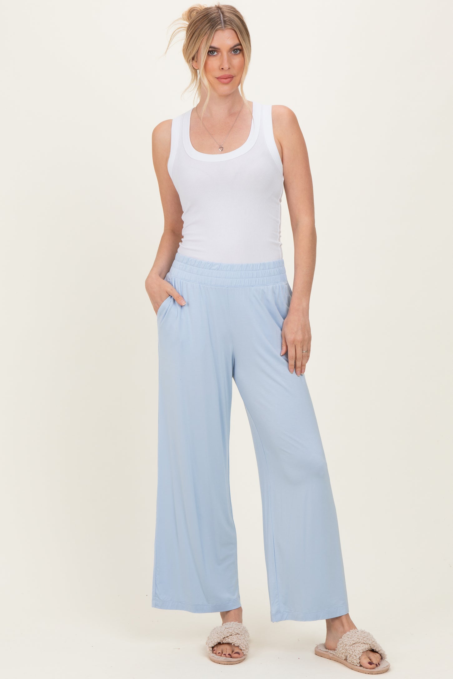 woman wearing a white ribbed tank top and light blue wide-leg pants, standing with hands in pockets