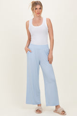 woman wearing a white ribbed tank top and light blue wide-leg pants, standing with hands in pockets