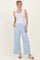 woman wearing a white ribbed tank top and light blue wide-leg pants, standing with hands in pockets