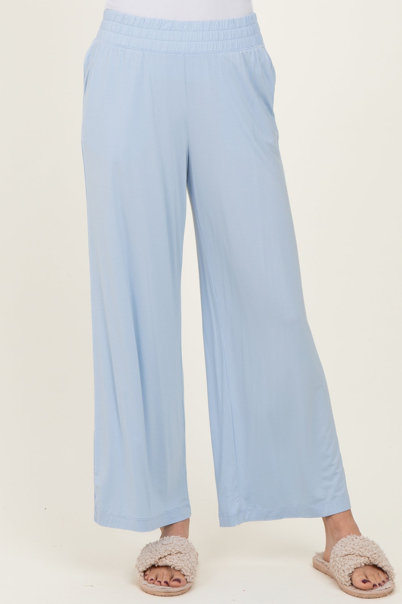 woman wearing light blue wide-leg lounge pants with an elastic waistband and side pockets, paired with fuzzy slippers