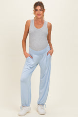 woman wearing a gray tank top and light blue maternity jogger pants with pockets, standing against a neutral background