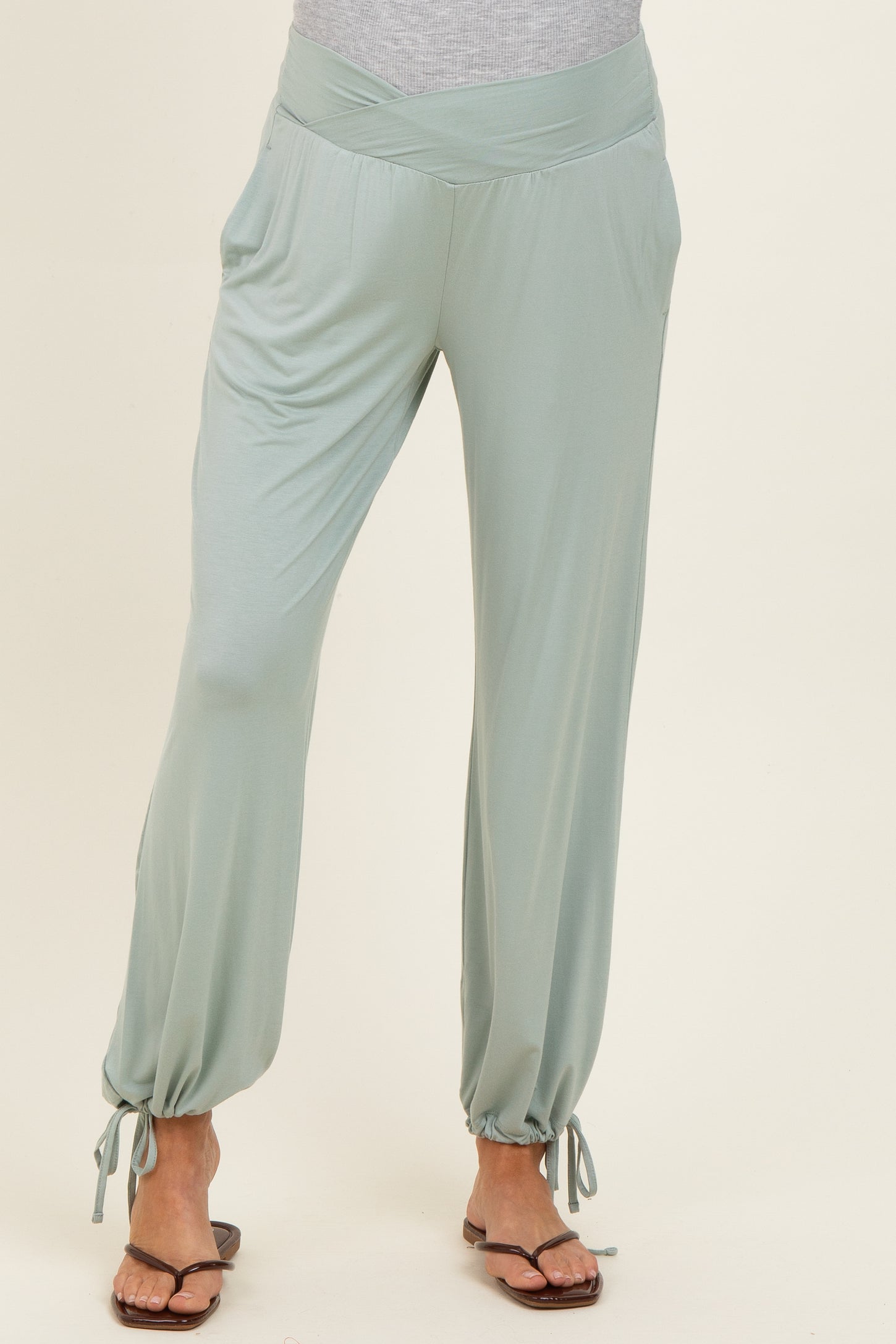 woman wearing light green maternity pants with a wide waistband and adjustable ties at the ankles