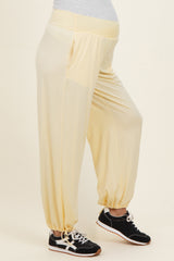 woman wearing light yellow maternity jogger pants with a stretchy waist and gathered cuffs, showcasing a baby bump