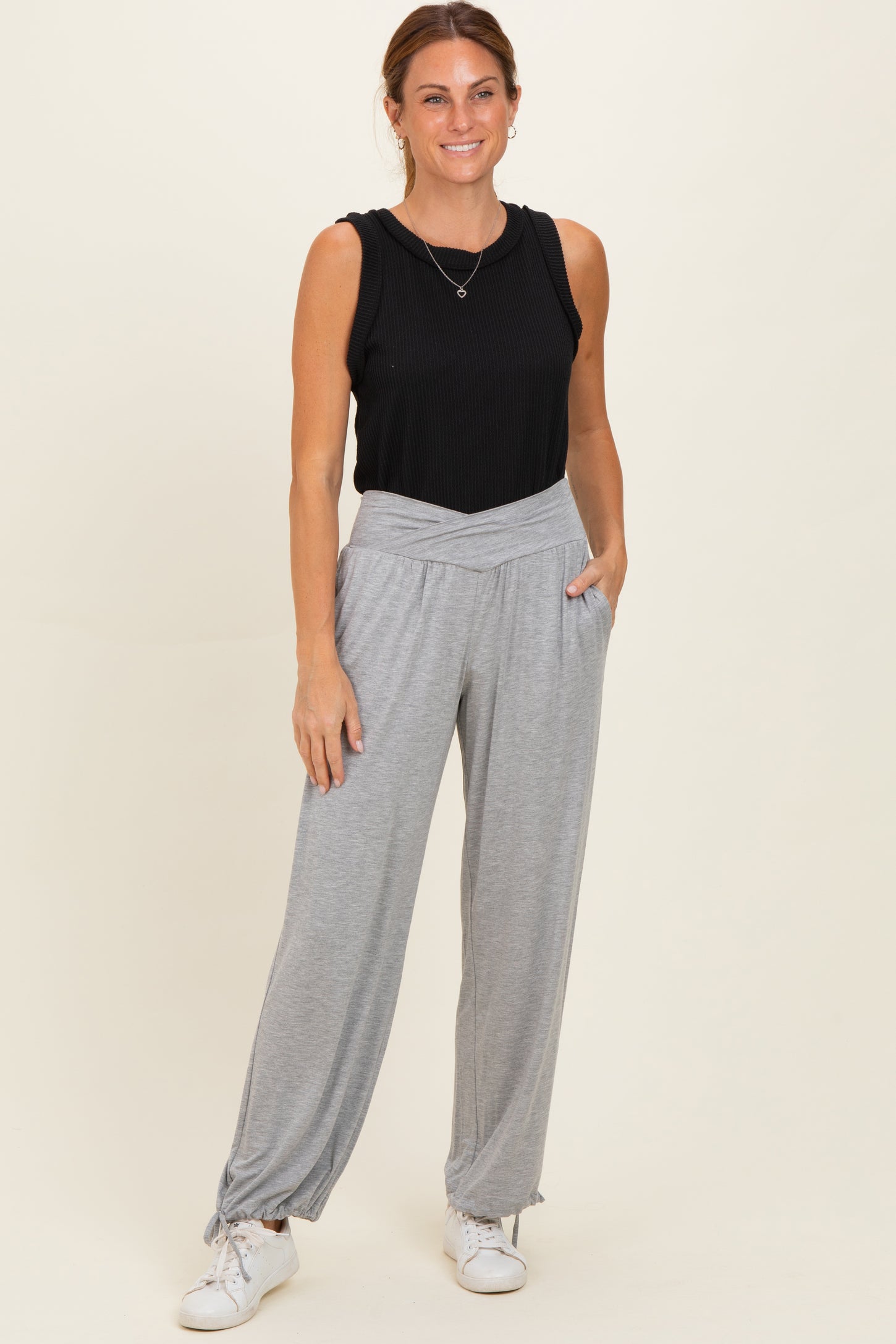 woman wearing a black sleeveless top and light gray wide-leg pants with side pockets, standing against a neutral background