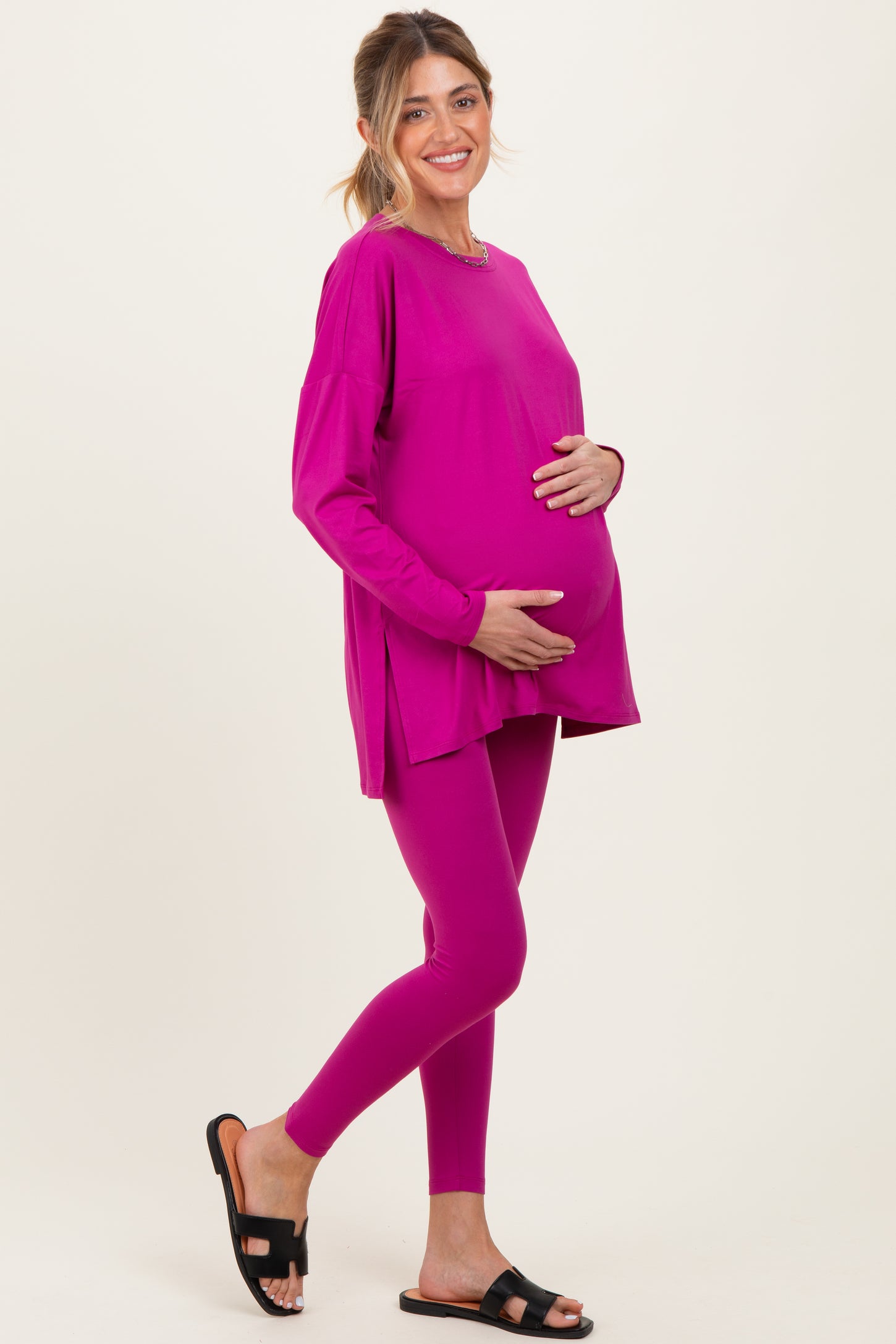 woman wearing a bright pink maternity top and leggings, showing her baby bump while posing with one hand on her belly