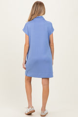 woman wearing a blue short sleeve maternity dress, viewed from the back, with a relaxed fit and above-the-knee length